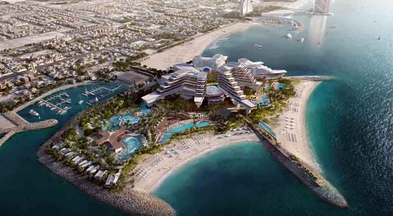 Vue aérienne d'une luxueuse station balnéaire avec plusieurs bâtiments, des jardins luxuriants, des piscines et une marina, nichée sur une péninsule sablonneuse sur fond de ville de Dubaï.