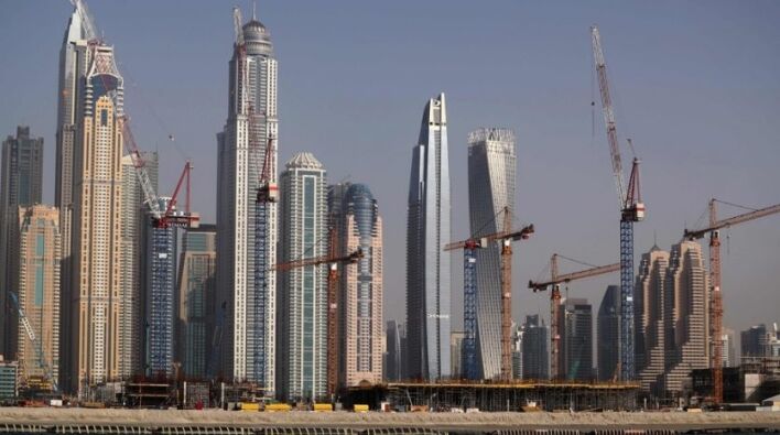 Horizon de gratte-ciel modernes en construction par un promoteur immobilier à Dubaï avec plusieurs grues, sur un ciel bleu clair et vu de l'autre côté de l'eau.