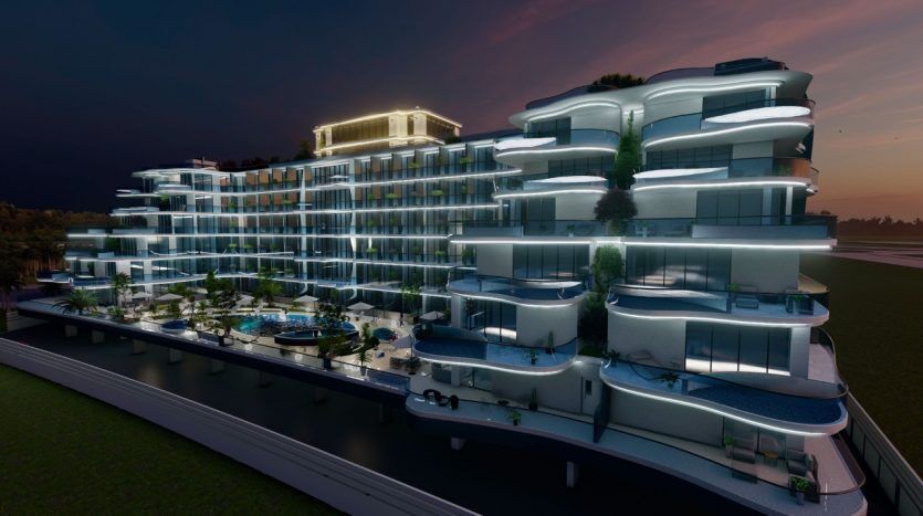 Un bâtiment de luxe moderne à plusieurs niveaux éclairé au crépuscule, doté de balcons spacieux avec de la verdure, des courbes architecturales élégantes et un toit proéminent, situé à côté d'une voie navigable tranquille dans le parc Samana.