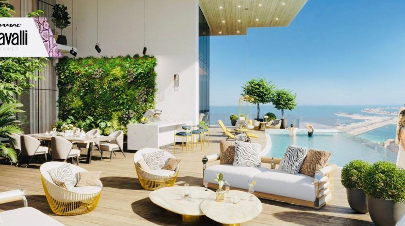 Luxurious rooftop terrace with elegant outdoor furniture overlooking the sea, featuring lush greenery and a woman looking out over the view. Roberto Cavalli Dubai tower logo visible.