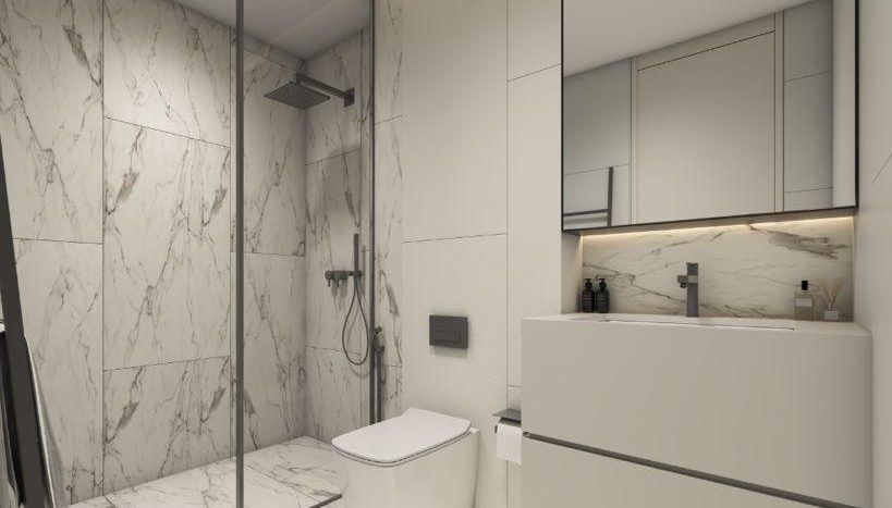Une salle de bains moderne avec des murs et des sols en marbre, comprenant une douche en verre, des toilettes blanches et une vasque avec un grand miroir éclairé par des plafonniers à Regalia Dubai.