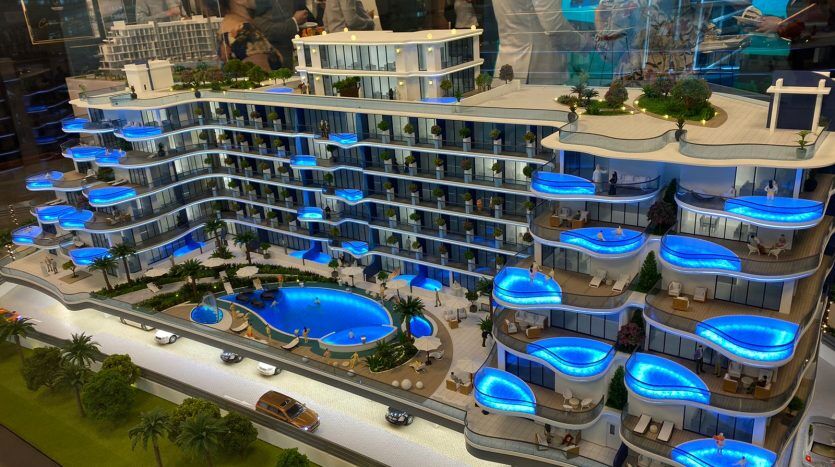 Un modèle détaillé d'un hôtel de luxe moderne comportant plusieurs niveaux avec des balcons bleus éclairés, entourant une piscine centrale, présenté lors d'une exposition à Dubaï avec des spectateurs.