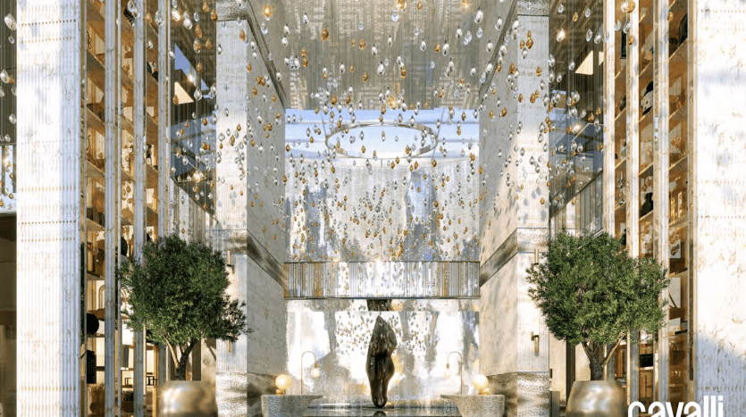 Located in Dubai's iconic Roberto Cavalli Tower, this luxurious, modern-design lobby features large mirrors, intricate lighting with numerous decorative hanging bulbs, large green plants and a black-and-white geometric-patterned floor. The Cavalli Tower logo is displayed in the corner.