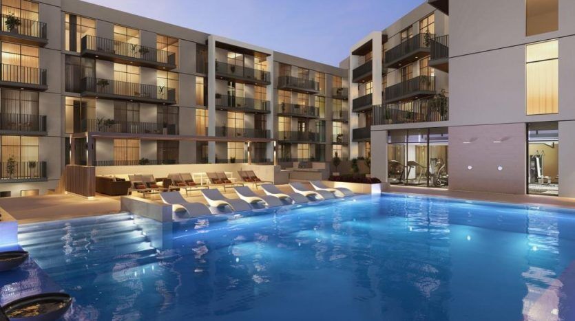 Une vue en soirée de Harrington House, un complexe d'appartements moderne doté d'une grande piscine. Au bord de la piscine se trouvent plusieurs chaises longues et des torches allumées. Le bâtiment dispose de balcons, certains avec de la lumière visible à l'intérieur