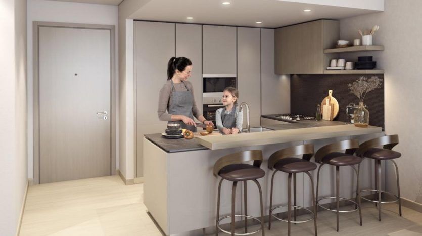 Une femme et une jeune fille dans la cuisine de la maison Harrington, avec la femme tenant un gâteau près d'un îlot avec des tabourets de bar. Espace lumineux et bien organisé.