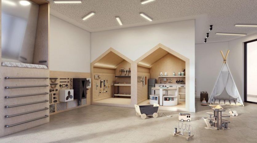 Salle de jeux pour enfants spacieuse dans la maison Harrington comprenant deux structures de jeu en bois en forme de maison, un tipi, un mur d'escalade et divers jouets en bois, éclairés par des plafonniers dans un cadre moderne.