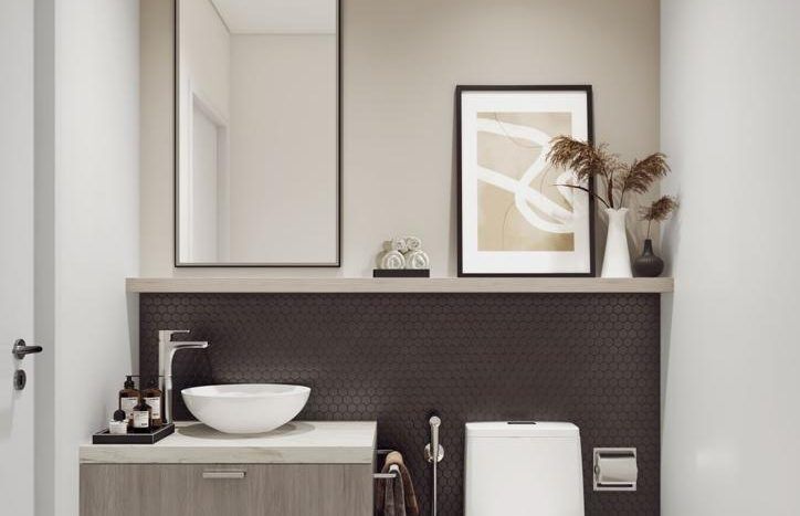 Une salle de bains moderne dans Harrington House comprenant des toilettes élégantes à côté d'une vanité en bois avec un lavabo et des articles de toilette. Un miroir encadré et des œuvres d'art abstraites sont suspendus au-dessus, complétés par des plantes en pot.