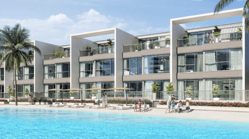 Des immeubles résidentiels modernes dotés de grands balcons surplombent un lagon bleu scintillant de Dubaï, entourés de palmiers et de personnes pratiquant diverses activités comme la natation et les bains de soleil.