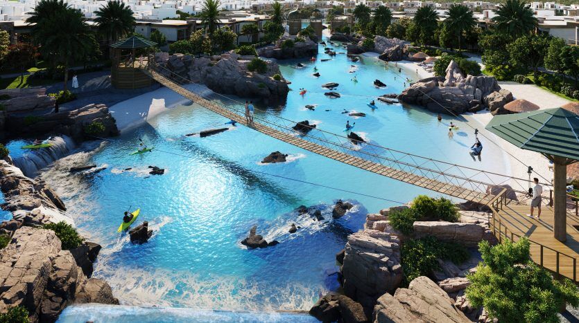 Une scène de villégiature animée à Dubaï, avec des gens faisant du kayak et marchant sur un pont de corde traversant un grand lagon artificiel turquoise entouré de verdure luxuriante et de formations rocheuses.
