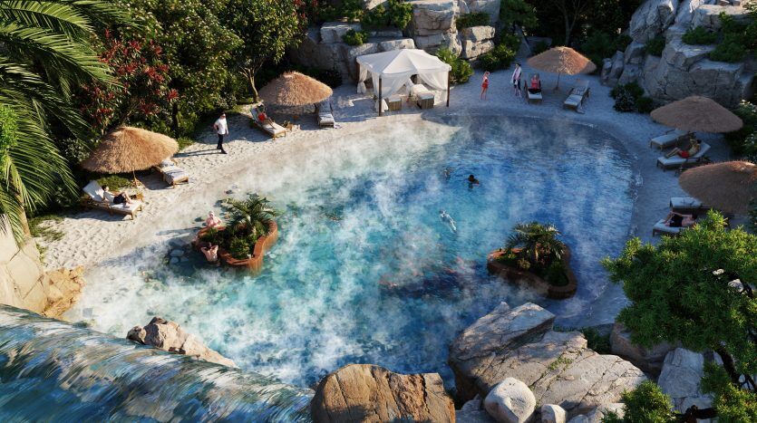 Vue aérienne de la piscine du complexe Damac Lagoons Costa Brava entourée d'une verdure luxuriante et de rochers, avec des gens qui aiment nager et se prélasser sous des parasols.