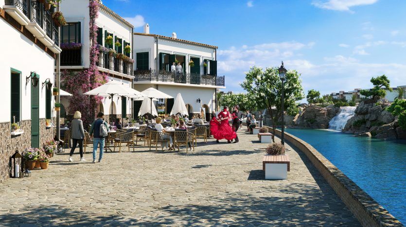 Une salle à manger pittoresque au bord de l’eau où les gens prennent leurs repas sous des parasols. Une danseuse de flamenco vêtue d'une robe rouge vif se produit près d'une cascade, à côté de bâtiments blancs de style méditerranéen aux volets verts représentés par un ag