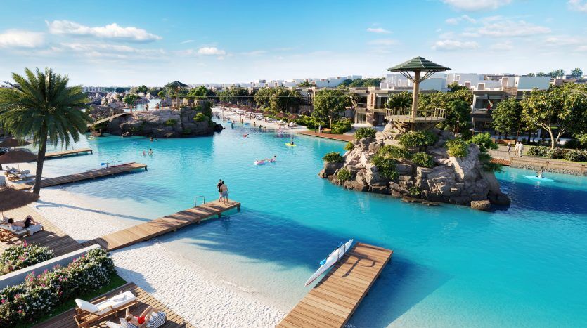 Une vue grand angle sur les luxueuses lagunes de Damac de la Costa Brava, comprenant plusieurs piscines, des formations rocheuses artificielles, des palmiers et des espaces de détente, où les clients peuvent profiter de diverses activités nautiques.