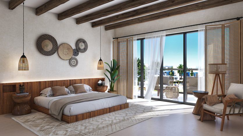 Une chambre moderne et spacieuse dotée d'un plafond aux poutres apparentes, d'un grand lit, d'œuvres d'art murales tissées et de portes coulissantes en verre ouvrant sur un balcon avec vue sur les lagons de Damac, Costa Brava.