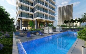 Un immeuble résidentiel moderne de grande hauteur avec une grande piscine extérieure entourée d'un aménagement paysager luxuriant et de chaises longues sous un ciel dégagé de Dubaï.