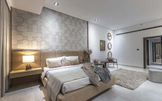 Moderna camera da letto in una villa di Dubai con letto matrimoniale, due comodini con lampade, pannelli decorativi alle pareti e varie opere d'arte. I colori neutri e il tappeto shag aggiungono calore all'ambiente spazioso.
