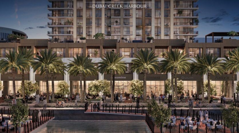 Illustration of the Creek Palace in Dubai Creek Harbour: a high-rise building with ground-floor apartments adorned with palm trees, open-air restaurants and well-lit pathways at night, bearing the Emaar name.