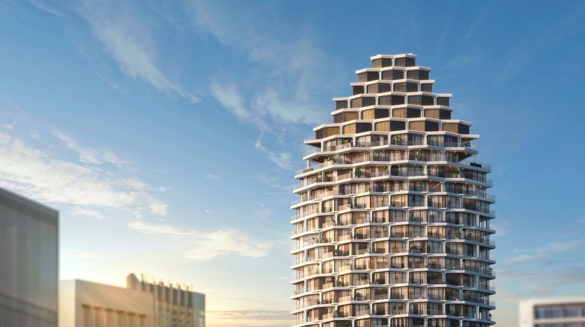 Un immeuble de grande hauteur moderne et cylindrique avec plusieurs balcons à chaque étage, sur fond de ciel bleu clair avec de légers nuages au coucher du soleil. L'architecture présente une série de niveaux en terrasses blancs, idéal pour