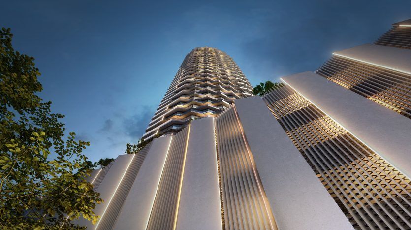 Vue en contre-plongée d'un gratte-ciel moderne à Dubaï au crépuscule, présentant une façade géométrique détaillée avec des lumières ambiantes, flanquée d'autres grands bâtiments sous un ciel crépusculaire.