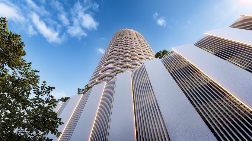 Vue en contre-plongée de gratte-ciel modernes aux conceptions architecturales uniques et superposées sur un ciel bleu clair, partiellement masqué par la cime des arbres verdoyants de Dubaï.