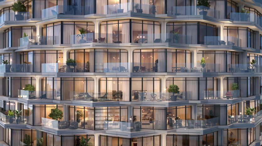 Gros plan d'un immeuble résidentiel moderne de grande hauteur à Dubaï au crépuscule, mettant en valeur son architecture incurvée et ses multiples balcons vitrés avec des lumières allumées.
