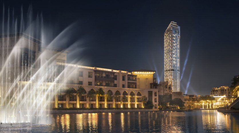 Vue nocturne d'un front de mer animé de Dubaï avec des fontaines illuminées, des villas élégantes et une tour saisissante se reflétant sur une rivière calme.