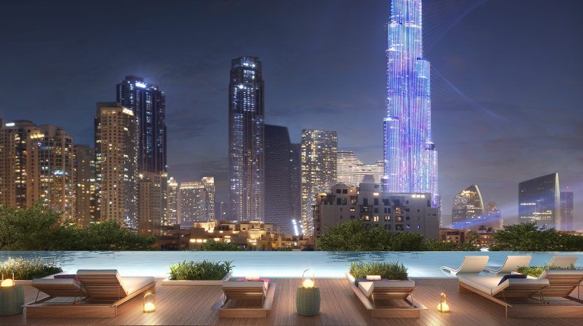 Une luxueuse piscine à débordement sur le toit surplombant un paysage urbain animé la nuit, avec des gratte-ciel illuminés et une tour proéminente perçant le ciel, flanquée de palmiers et de chaises longues dans un immobilier exclusif de Dubaï
