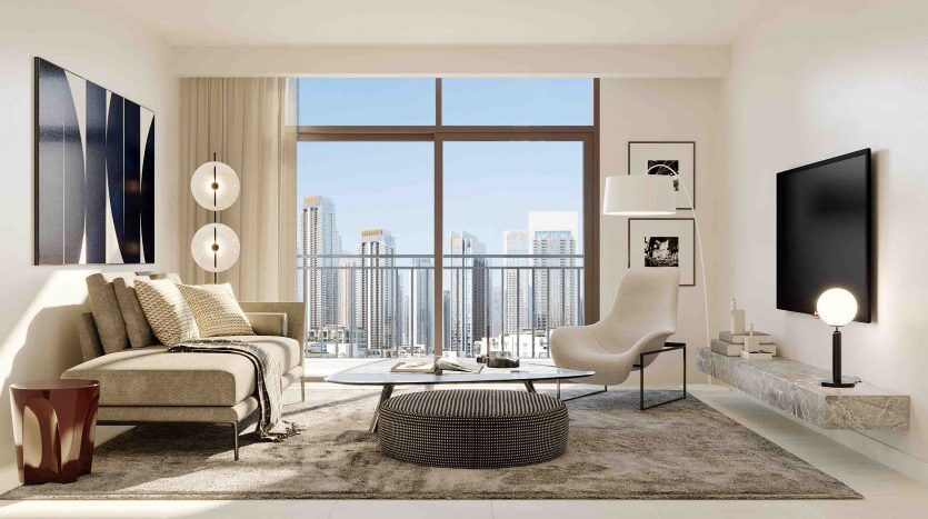 A modern living room in a Dubai apartment with a beige sofa, a round black coffee table, a white armchair and a large window overlooking a cityscape. The decor includes a floor lamp and a shelf,