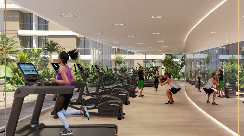 Une salle de sport moderne et bien équipée dans une villa de Dubaï avec divers appareils d'exercice et des personnes qui s'entraînent, dont une femme sur un tapis roulant au premier plan. La lumière naturelle illumine l'espace, rehaussée par les plantes d'intérieur