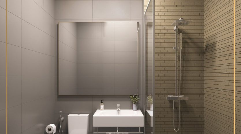 Salle de bains moderne dans une villa de Dubaï avec cabine de douche en verre, toilettes blanches et lavabo beige avec vanité. La pièce est éclairée par des plafonniers et présente des murs carrelés gris et beige.