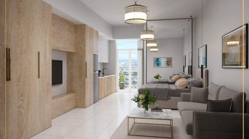 Un studio moderne à Dubaï avec un espace de vie intégré comprenant une cuisine, un coin repas et un salon, décoré dans des tons neutres avec des accents en bois et complété par la lumière naturelle.