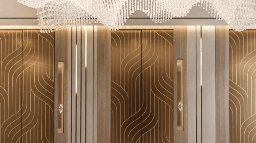 Luxurious lobby of a Dubai hotel featuring three elegant wooden elevator doors with artistic wave patterns, complemented by a sophisticated, expansive chandelier.