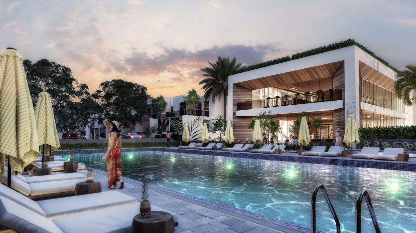 Un cadre luxueux au bord de la piscine au crépuscule avec une femme en robe rouge debout près d'une piscine éclairée, entourée de cabanes, de palmiers et d'une villa moderne à Dubaï en arrière-plan.