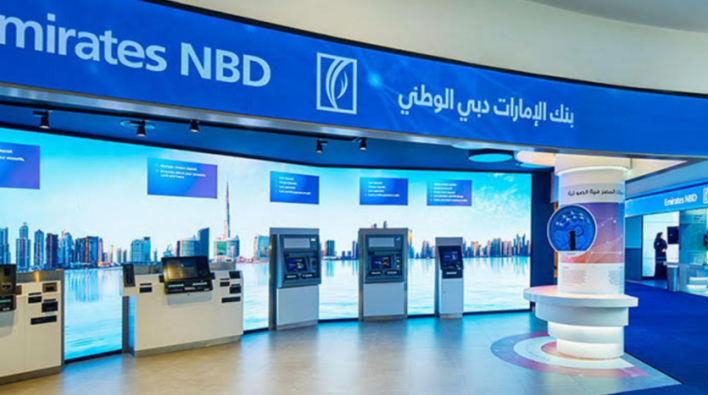 Interior of an Emirates NBD bank branch in a Dubai villa with several ATMs, a help desk and promotional displays under well-lit blue and white signage.