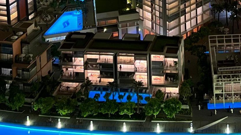 Vue aérienne d'une scène urbaine animée la nuit avec un bâtiment moderne avec des étages intérieurs éclairés, entouré d'arbres, une piscine bleue lumineuse et des gratte-ciel adjacents à Dubaï.
