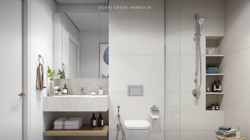 Intérieur de salle de bains moderne au design minimaliste comprenant une cabine de douche en verre, des murs blancs, des toilettes murales et un banc en bois sous un comptoir d'évier en marbre. La superposition de texte indique "Villa Dubaï - Dubaï