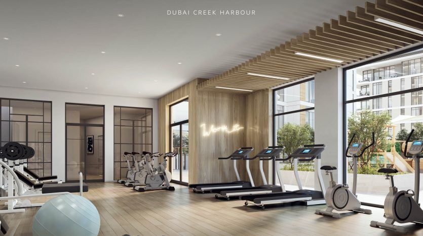 Intérieur de salle de sport moderne à « The Cove, Dubai Creek Harbour » comprenant des tapis roulants, des vélos d'exercice, des poids et de grandes fenêtres, avec une esthétique spacieuse et épurée dans le luxueux immobilier Dubai.