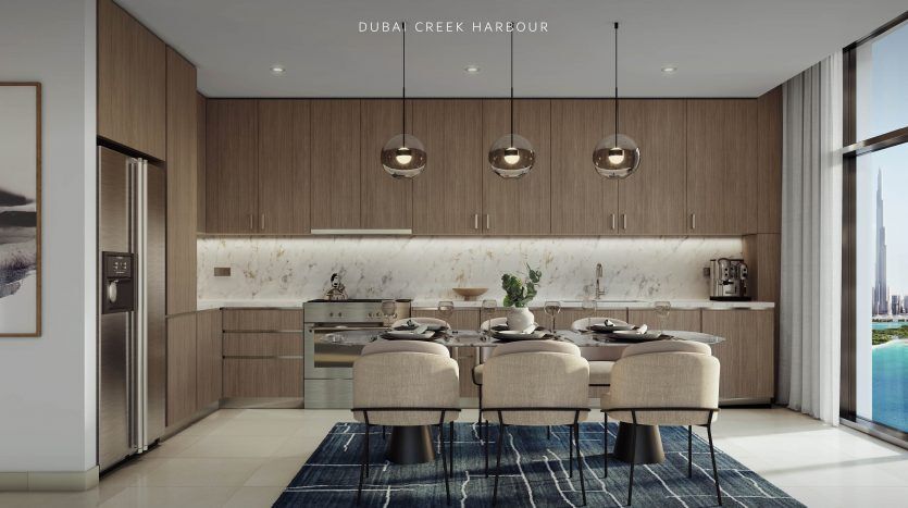 Une cuisine moderne avec des armoires en bois élégantes et des comptoirs en marbre avec un bar de petit-déjeuner avec des tabourets. De grandes fenêtres offrent une vue sur le front de mer. Texte : "Le port de Cove Dubai Creek. Emaar, Imm