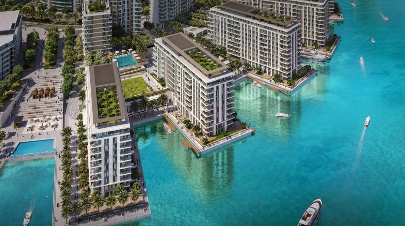 Vue aérienne d'un luxueux développement immobilier de Dubaï en bord de mer avec des immeubles modernes de grande hauteur entourés d'eau turquoise vibrante, avec une verdure luxuriante, des piscines et des bateaux naviguant à proximité.