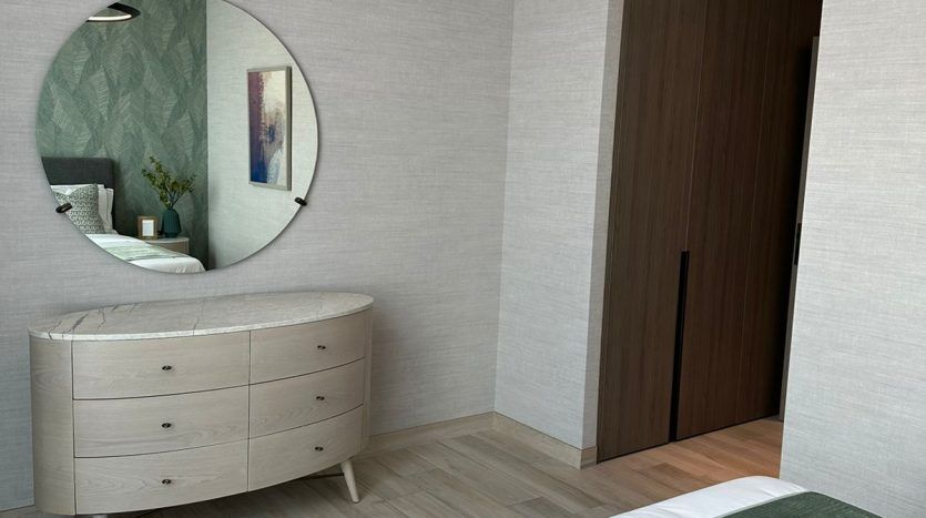 A modern bedroom in a Dubai villa with a carefully made bed with a green throw, a light wood dresser topped with a circular mirror and unique circular ceiling lights. Clean, neutral color palette.