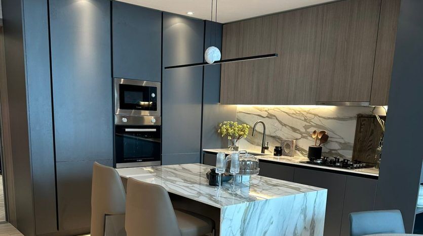 Modern kitchen in a Dubai villa with elegant gray cabinetry, marble countertops and a central island. Stainless steel appliances and minimalist suspension are visible.