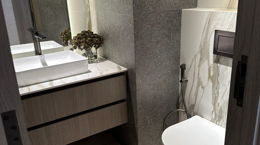 Modern bathroom in a Dubai apartment with wall-mounted toilet, wooden washbasin with rectangular basin and marble walls, seen from the door.