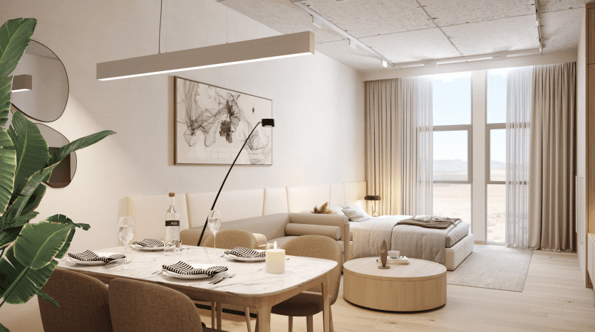 Modern studio in Dubai with an open-plan layout, including a dining area for two and an adjacent bedroom area with a double bed, large windows and minimalist decor.