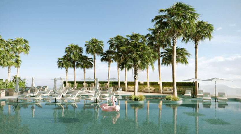 Luxurious rooftop pool with crystal-clear water, surrounded by tall palm trees and white sun loungers. A pink flamingo floats in the water and umbrellas provide shade nearby, under a clear blue sky.