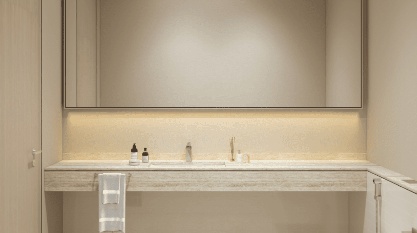 A modern bathroom featuring a large rectangular mirror above a long sink counter with various toiletries, a hanging white towel and a stylish toilet on one side. Soft lighting enhances the warm ambience, perfect for a cosy atmosphere.