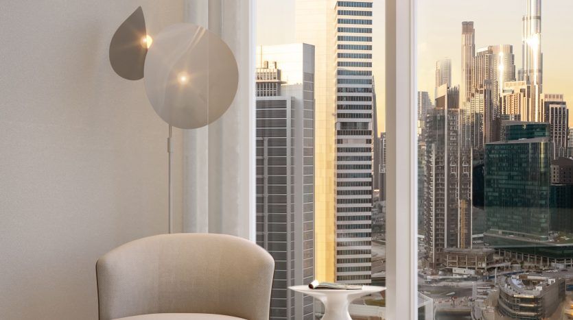 Un coin moderne et confortable dans un appartement de grande hauteur à Dubaï, doté d'une chaise et d'une lampe élégantes avec une vue panoramique sur les toits animés de la ville au coucher du soleil.