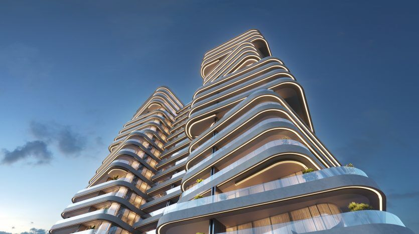 Un immeuble d'appartements futuriste de plusieurs étages à Dubaï avec des lignes architecturales ondulées et fluides sous un ciel bleu clair au coucher du soleil, mettant en valeur le design unique et moderne de la structure.