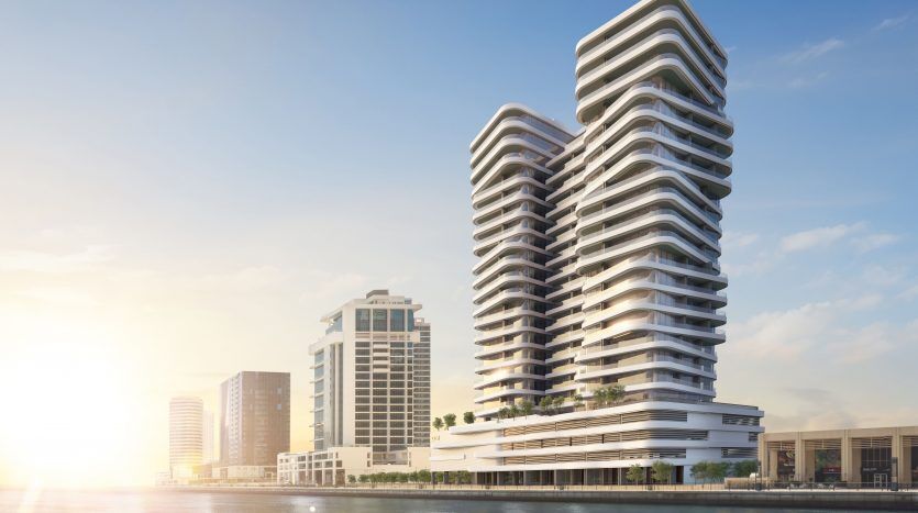 Bâtiments modernes en bord de mer à l'architecture incurvée sous un ciel clair à Dubaï, reflétant le lever du soleil sur les eaux calmes.