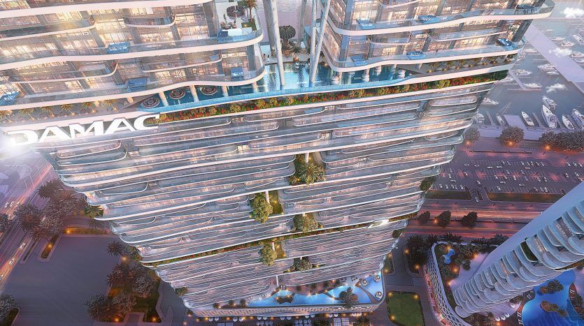 Un gratte-ciel futuriste au design ondulé unique, orné du nom « damac » au sommet, entouré d'une verdure luxuriante et d'autres bâtiments modernes au crépuscule, représente un investissement exclusif.