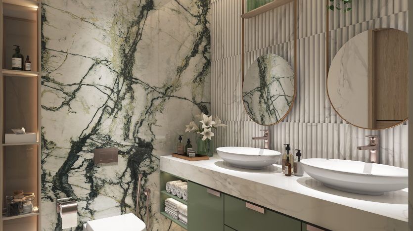 Une salle de bains moderne dans un appartement de Dubaï avec un mur en marbre vert saisissant, deux lavabos blancs sur une vanité couleur menthe, des miroirs ronds, des toilettes et des accents en bois avec de la verdure.