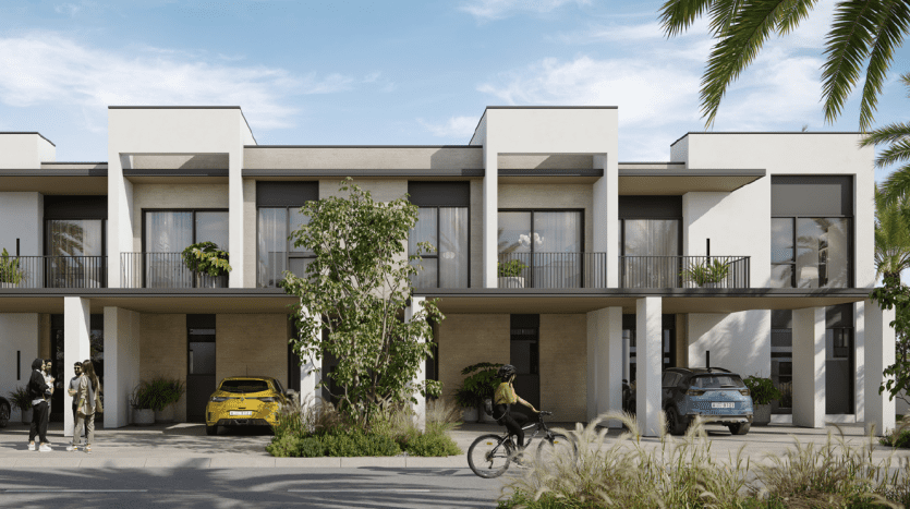 Complexe de villas modernes aux lignes épurées et aux couleurs neutres, avec résidents et véhicules à l'extérieur, entourés d'une verdure luxuriante et de palmiers sous un ciel dégagé.